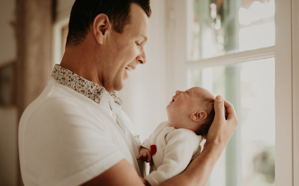 Papa tenant son nouveau-né près de la fenêtre à domicile