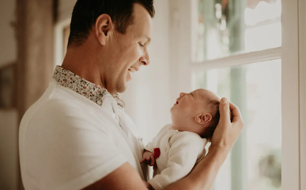 Papa tenant son nouveau-né près de la fenêtre à domicile